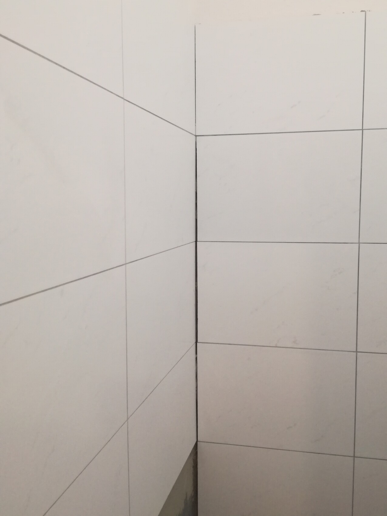 Corner view of two white wall tiles at a bathroom corner with gray grout lines.