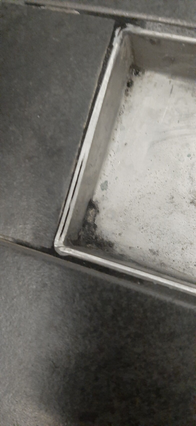 Close-up of a flat metal container with white powder dust in the corner.