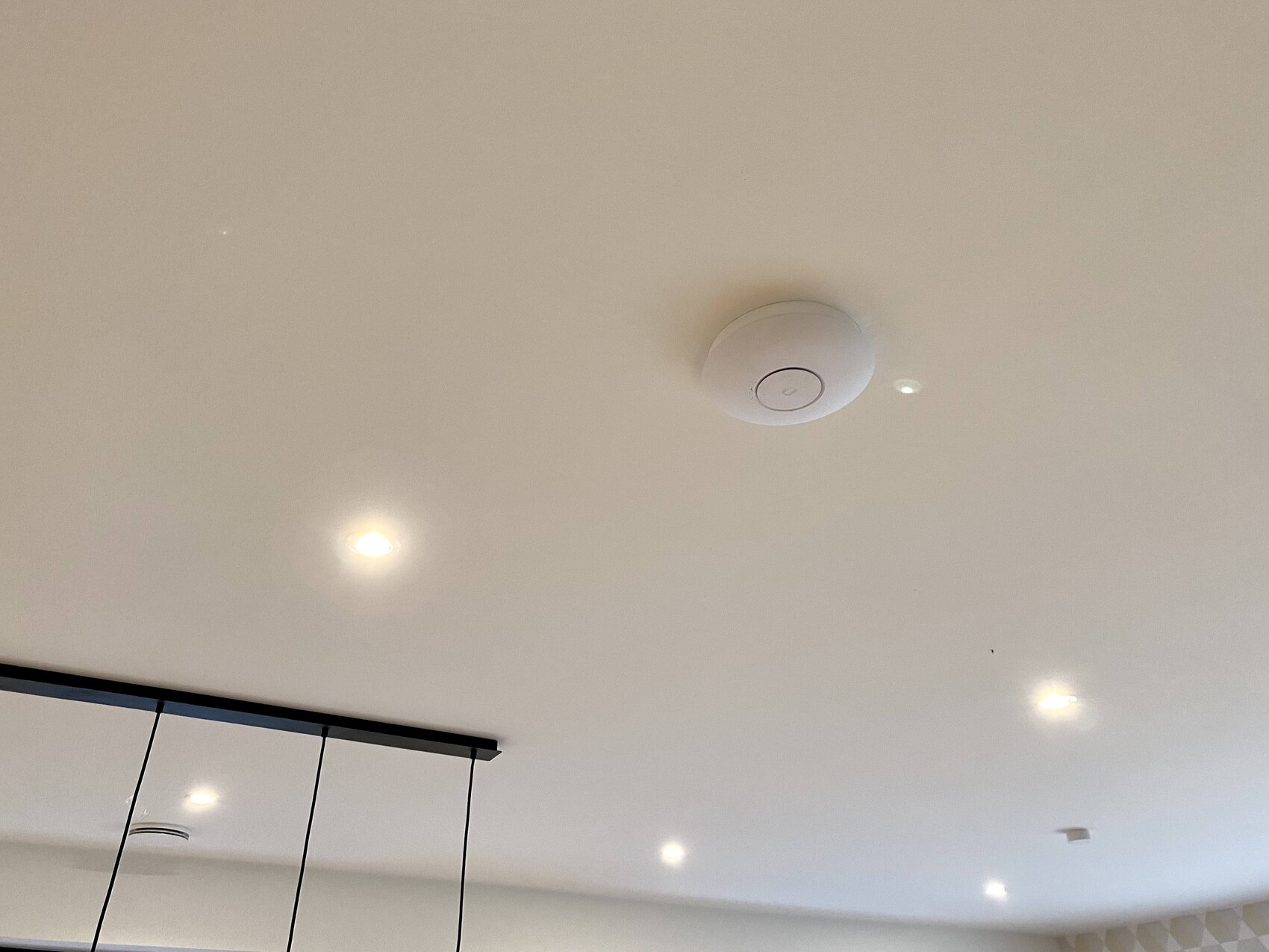 White ceiling with several downlights; central round smoke detector device, pendant strip on the left.