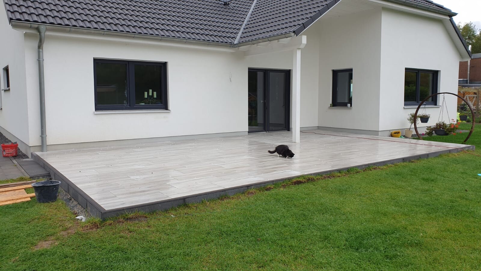 Modern white bungalow with large light gray terrace; small black animal on it