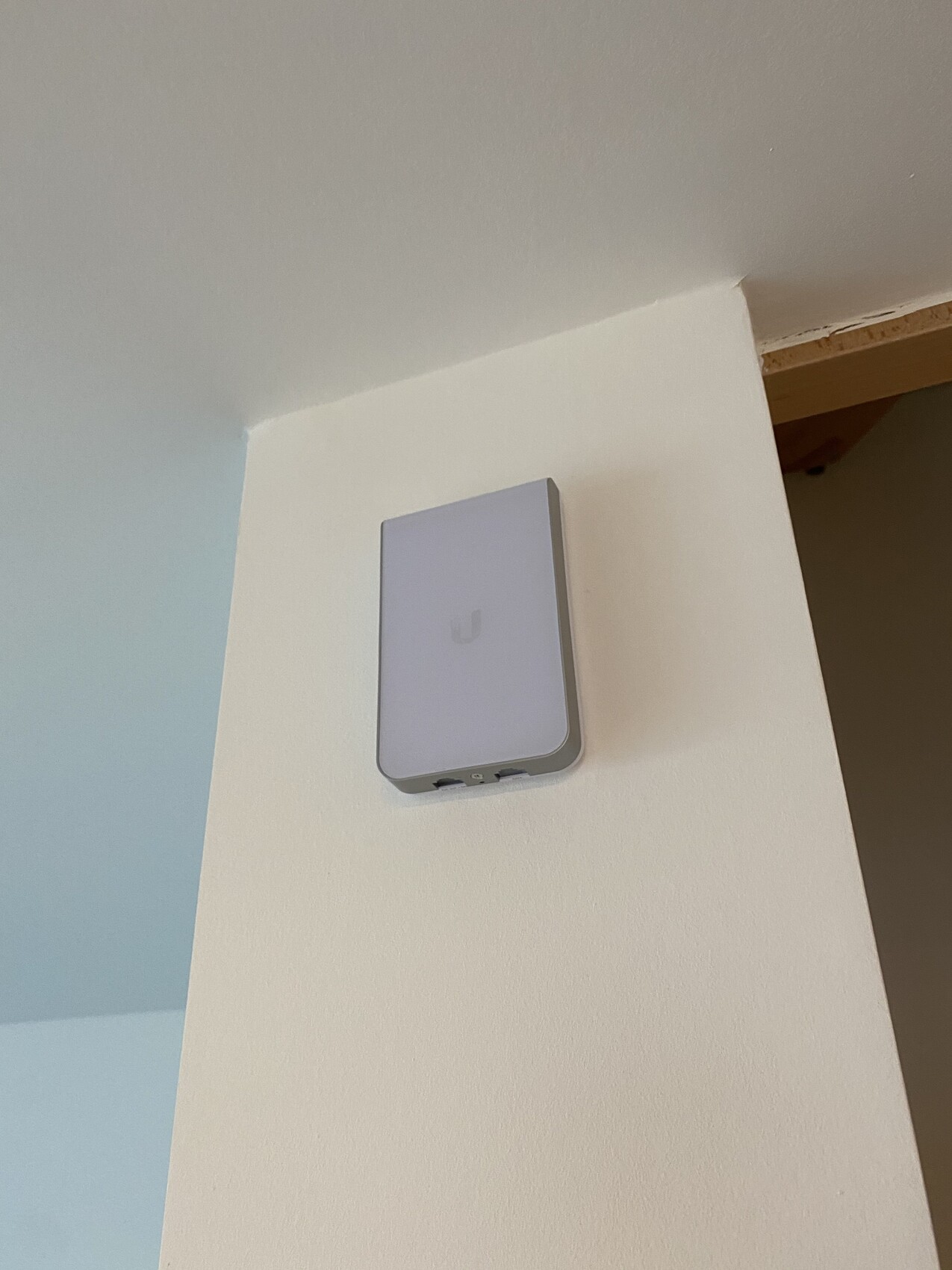 Small white wall device with rounded edges, presumably a Wi-Fi access point, mounted on the wall.