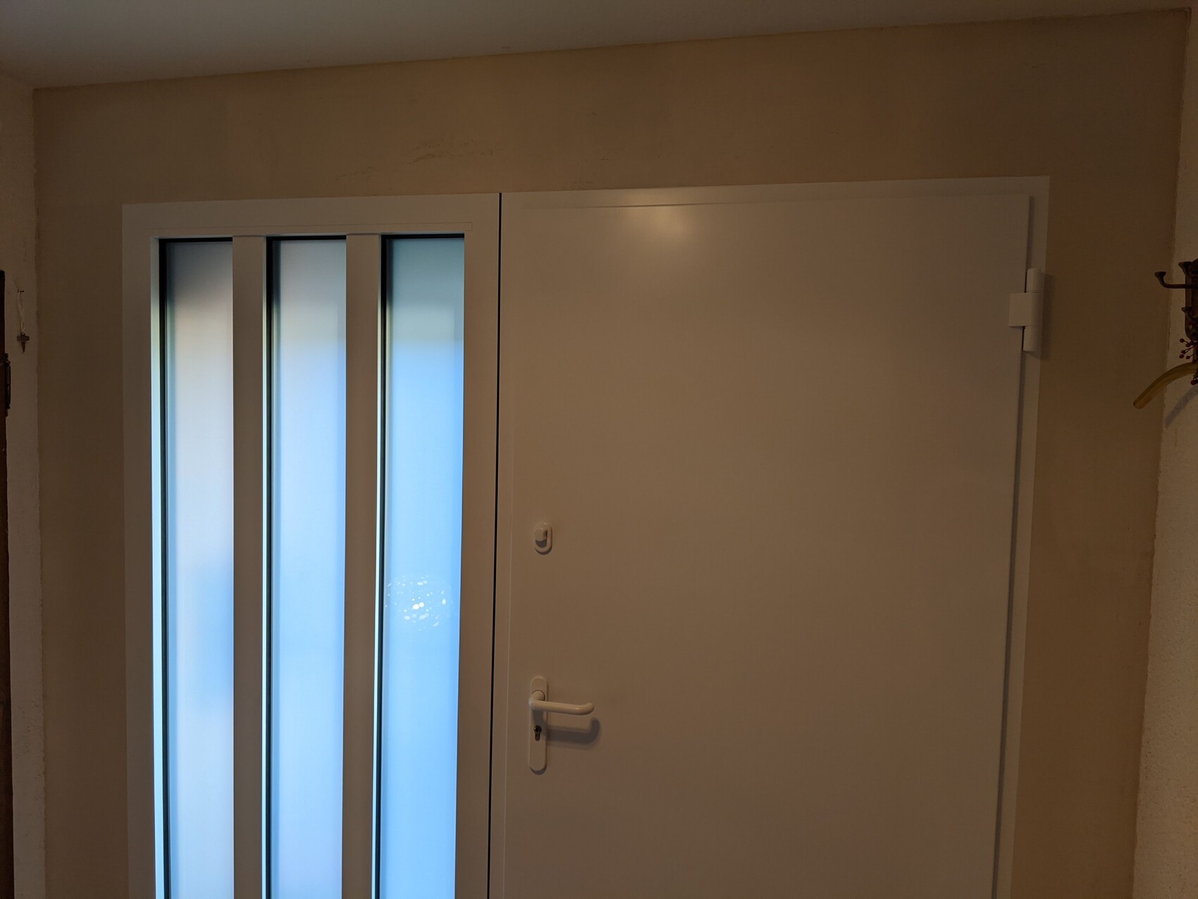 Weiße Tür mit vertikalen Glasfenstern links in einem beigen Flur; Türgriff rechts.