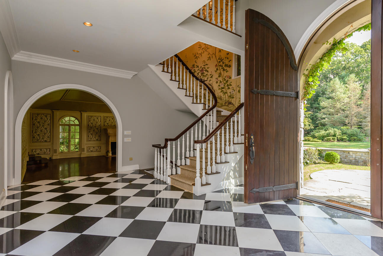 Large entrance area with staircase, checkerboard floor, and open wooden door leading to garden