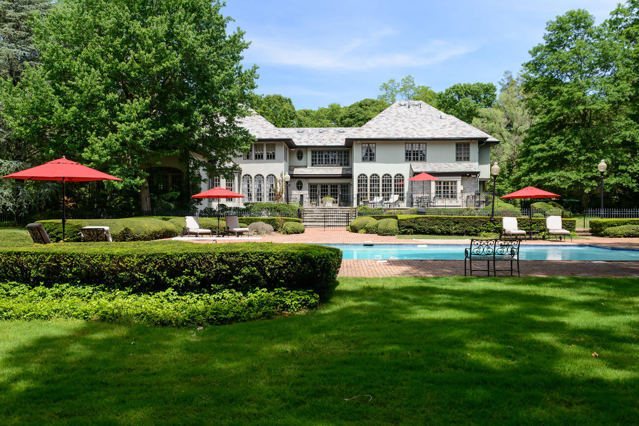 Large estate with pool, lounge chairs, red umbrellas, and manicured garden.