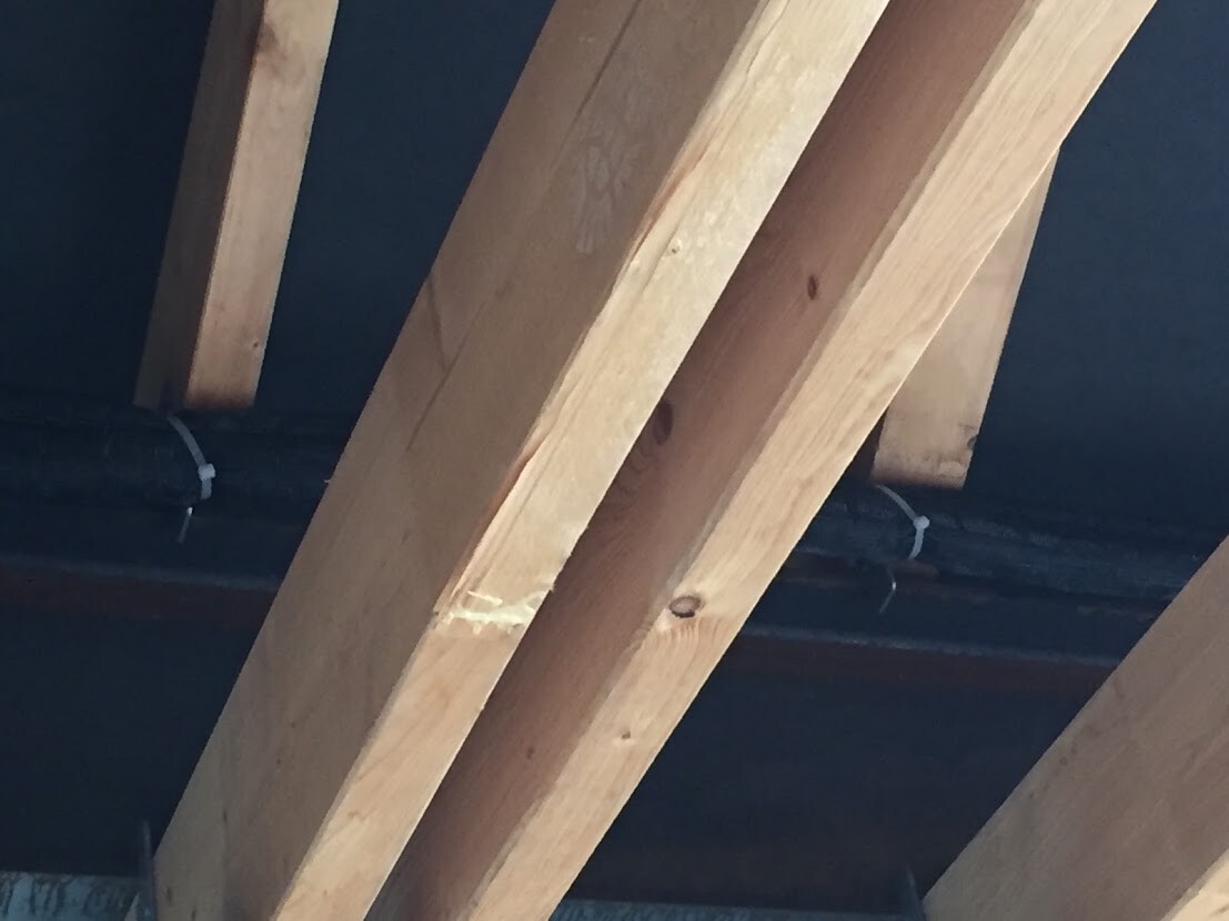 Roof structure with slanted wooden beams inside, dark background, visible cables