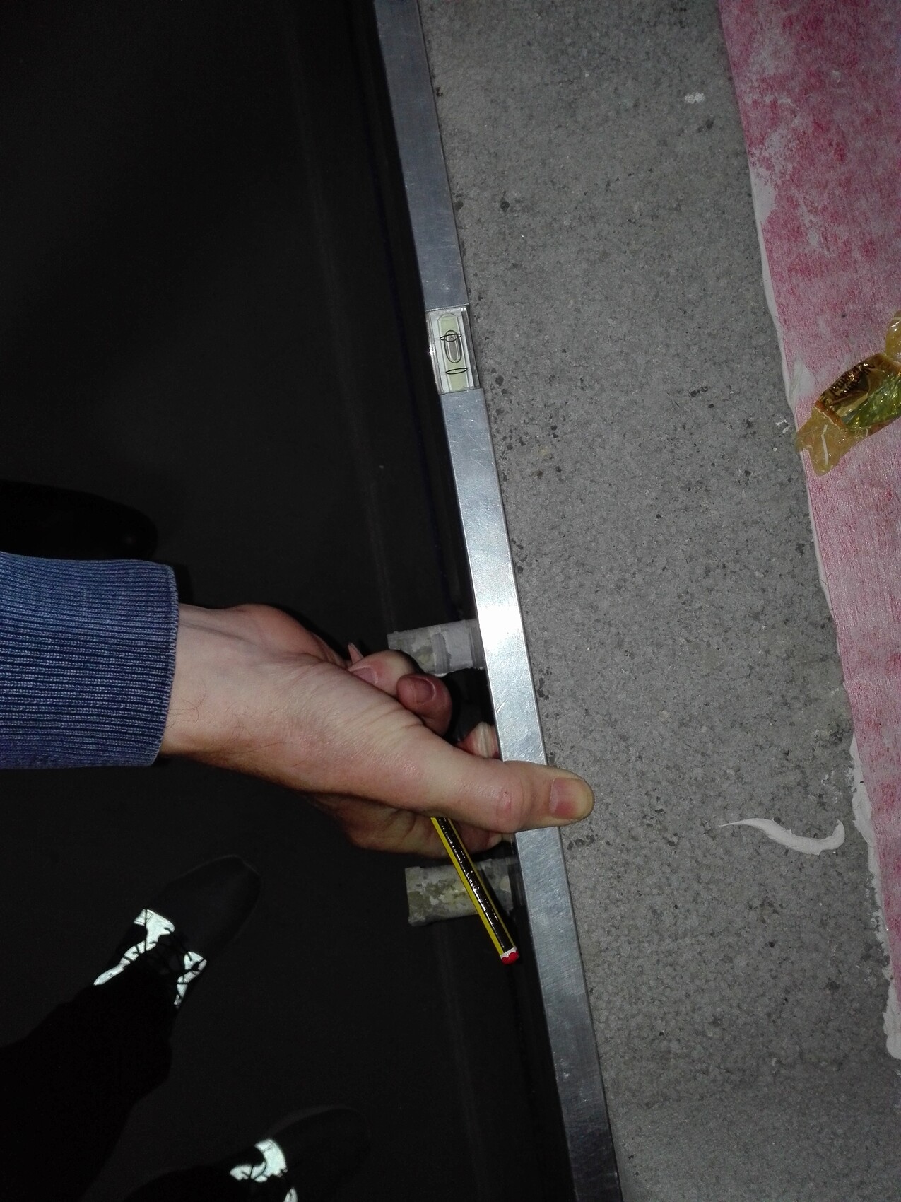 Hand with pencil on the edge of a metal frame on a concrete floor; small spirit level visible.