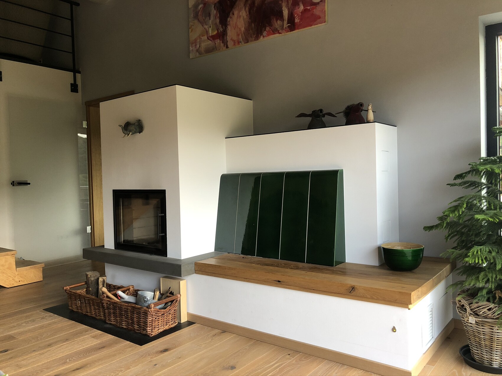 Modern living room with fireplace, wood basket, green tiles in front of white wall panel and plant.