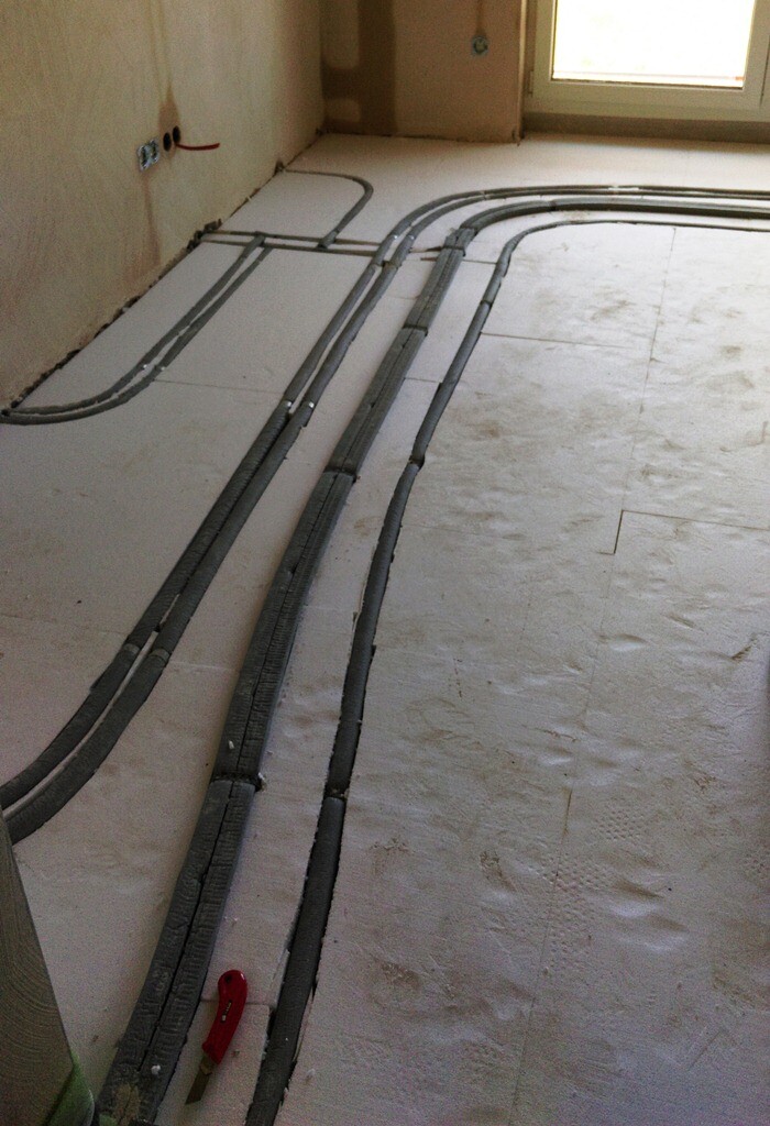 Cabling ducts lying on the unfinished floor of an interior room; windows in the background.