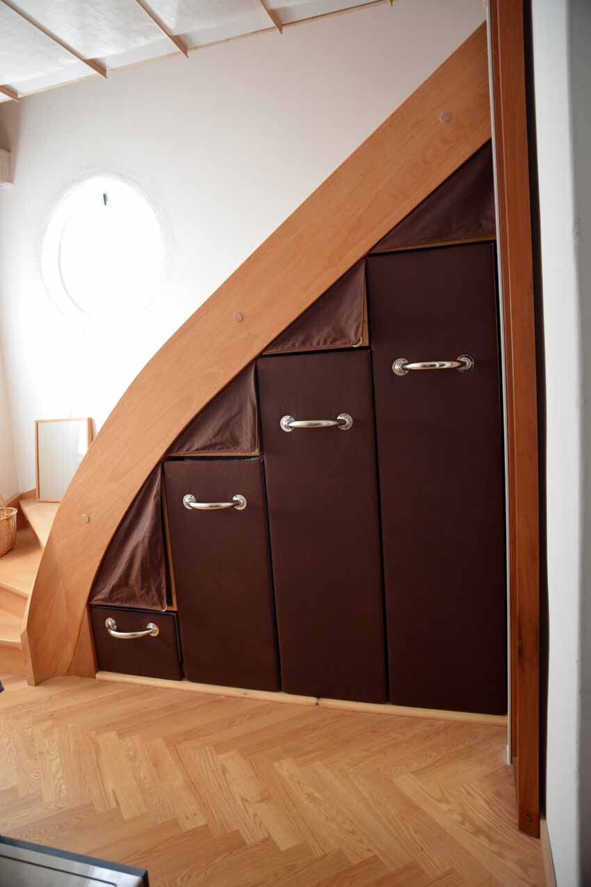 Brown cupboards with silver handles under the staircase on a wooden floor.