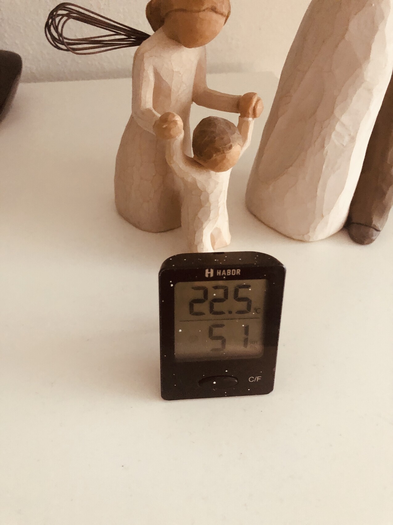 Wooden figurine group: mother holding child; next to it a digital thermometer showing 22.5°C and 51% humidity