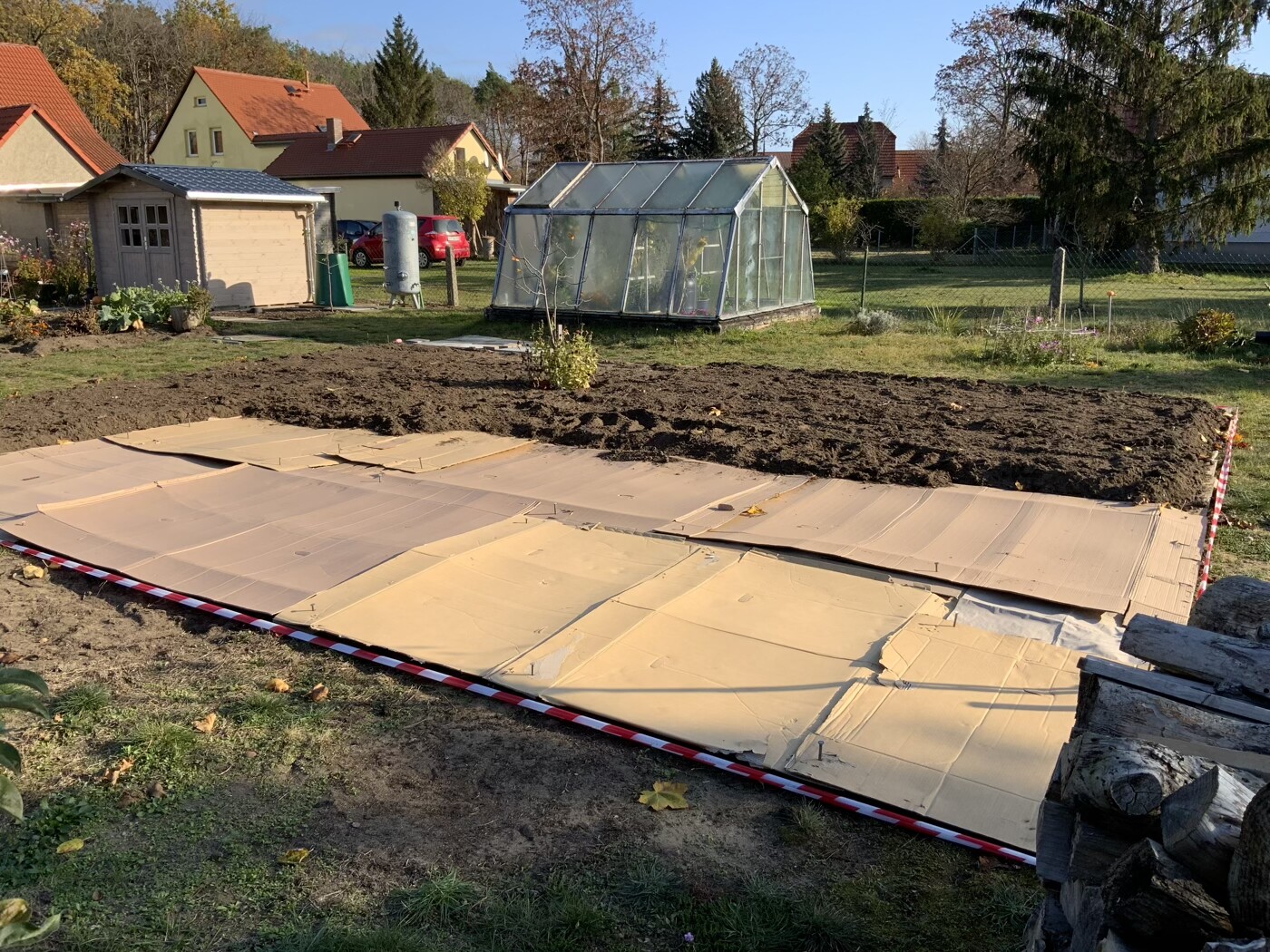 Grundstuecksvorbereitung-im-Garten-mit-Kartonplatten-und-Gewaechshaus-im-Hintergrund