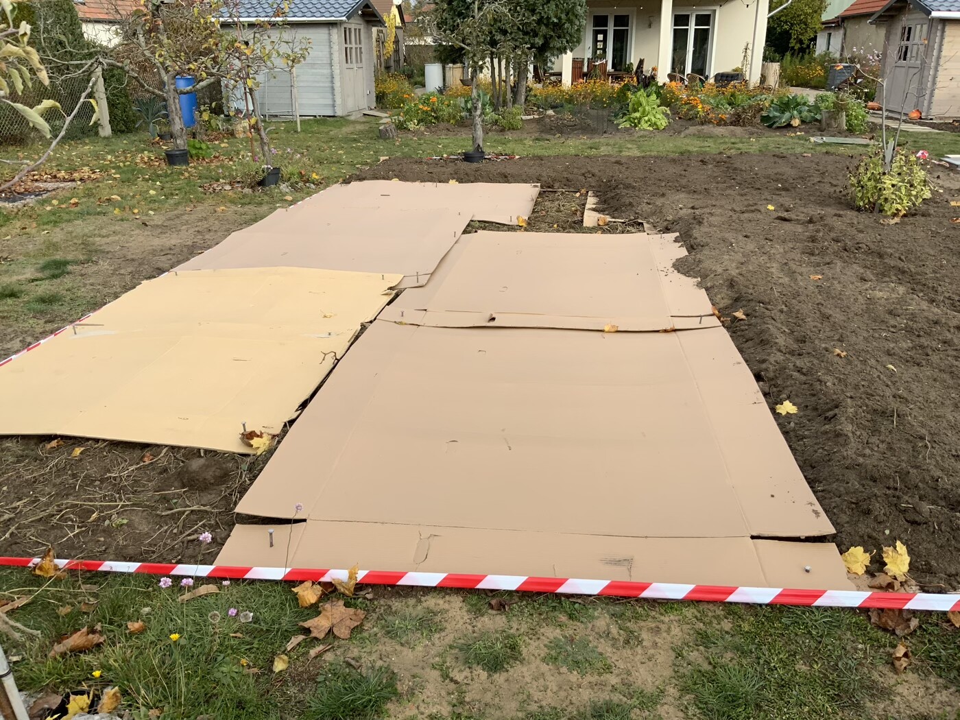 Provisorischer Kartonpfad im Garten über Erdarbeiten; Absperrband im Vordergrund.