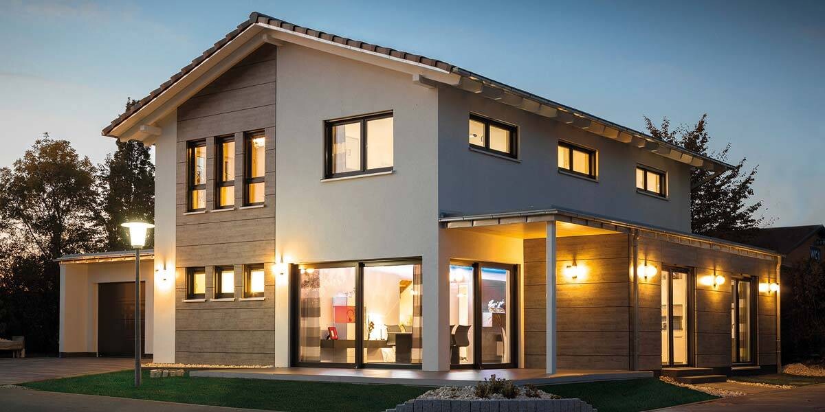 Modern two-story house with large window fronts, warmly illuminated interior, and outdoor lamps