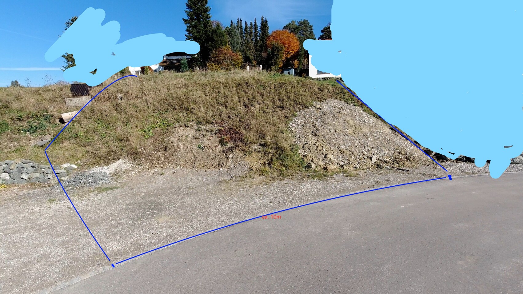 Steep gravel hill beside road, blue lines mark plot boundary; background trees.