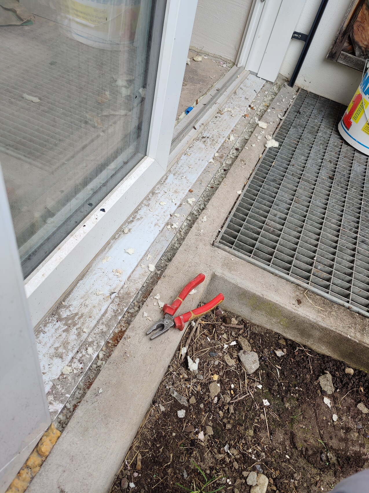 Rote Zange liegt an der Türschwelle neben der Glas-Schiebetür; draußen Schmutz und Kies.