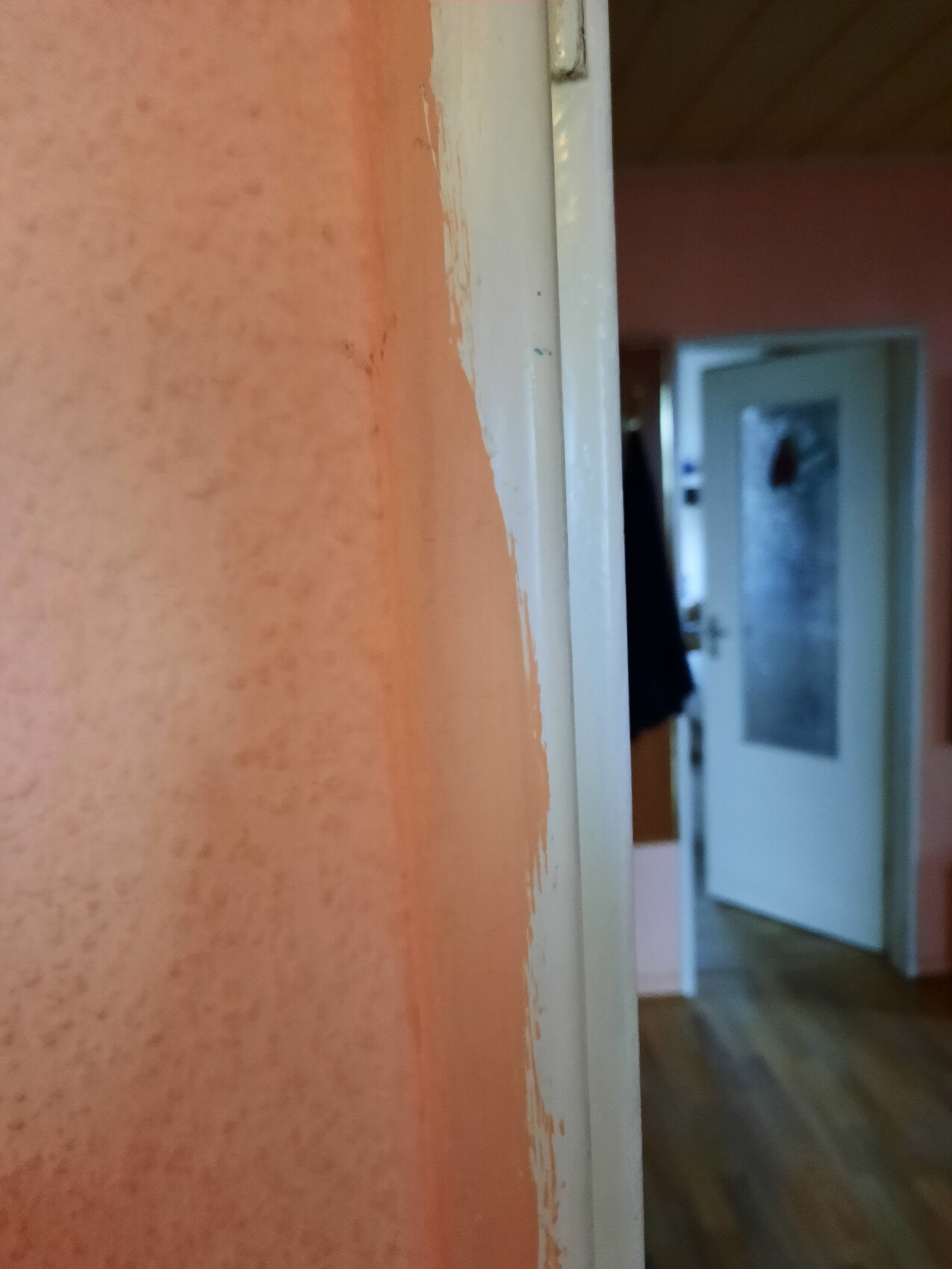 Close-up of an orange wall with peeling paint next to a white door frame; open door in the background.