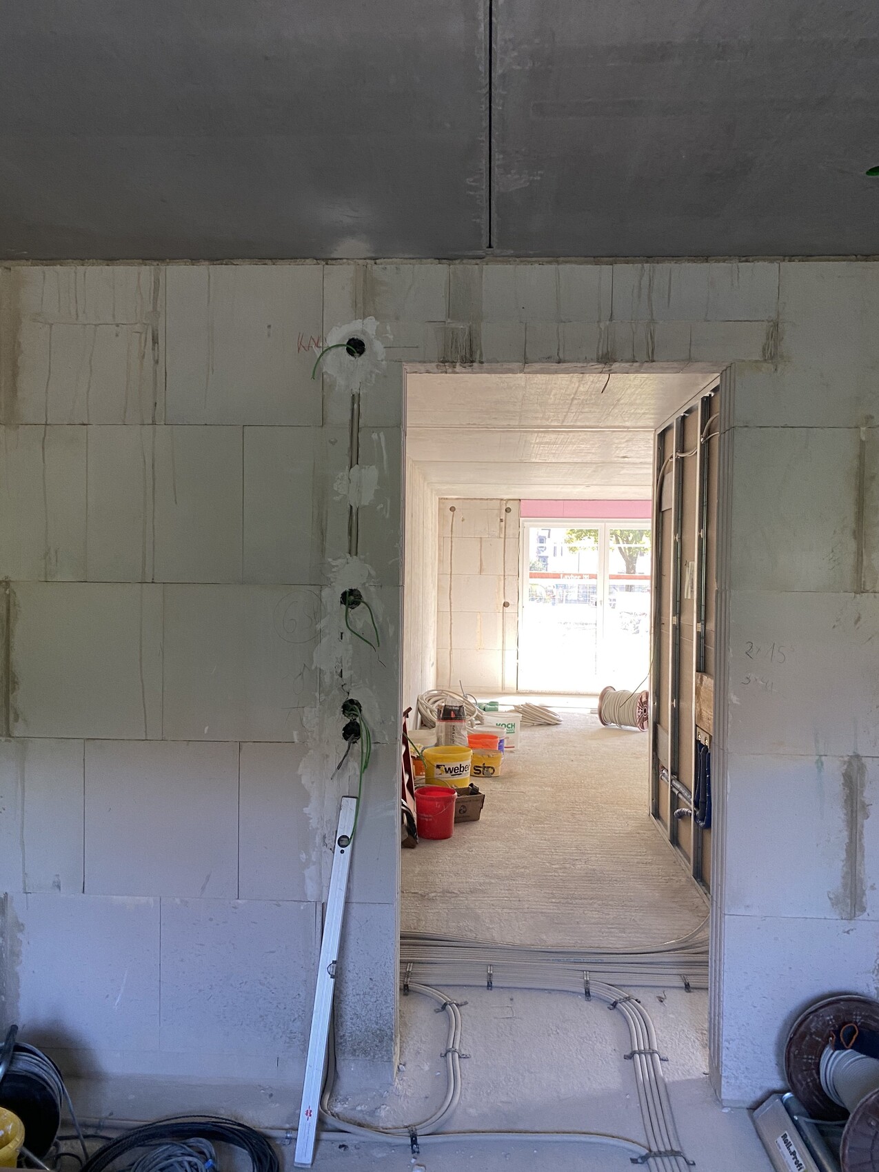 Construction site: Unplastered wall with exposed electrical cables; passageway to a bright room with windows.