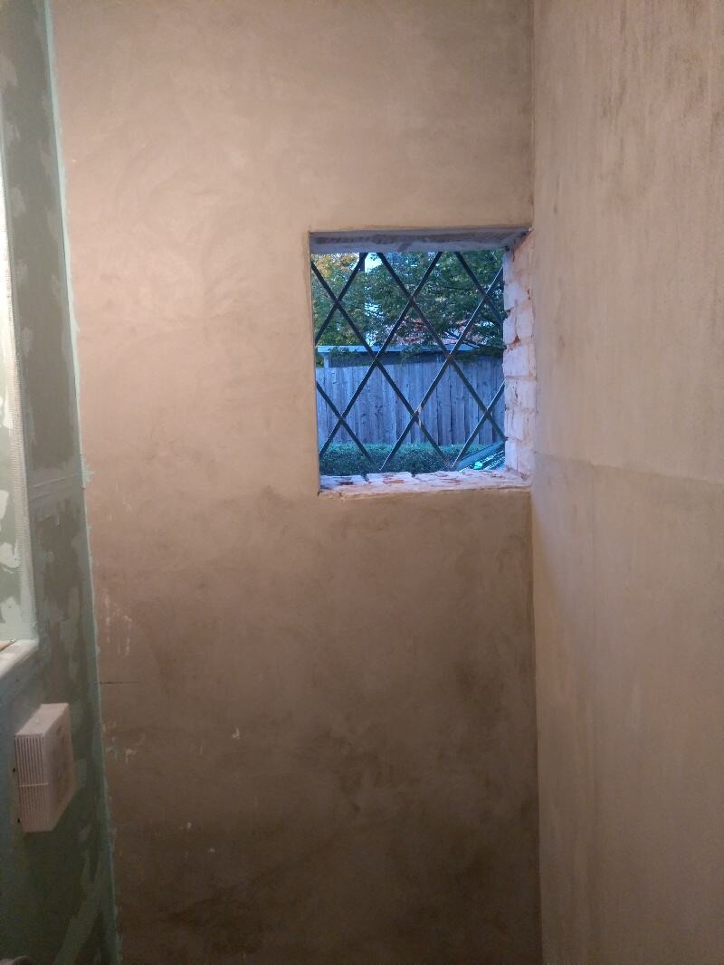 Interior of a construction site: small square window with a grille, view onto the garden.