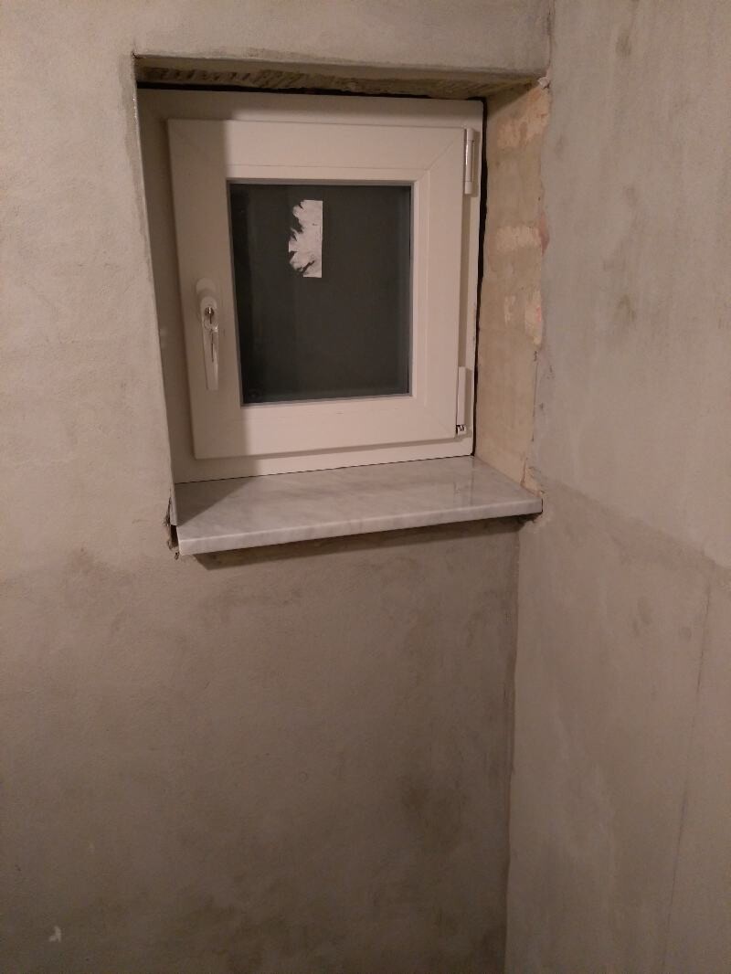 Small white window in a rough basement wall, stone sill below.