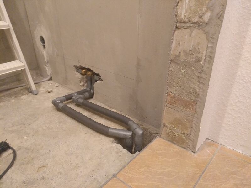 Grey PVC pipes in a U-shape on the wall; construction site with ladder, tiled floor