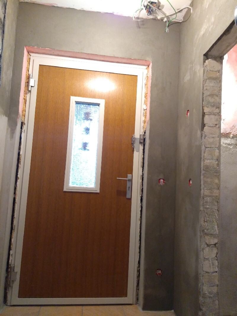 Wooden door with vertical glass window, unfinished wall, exposed cables, construction condition.