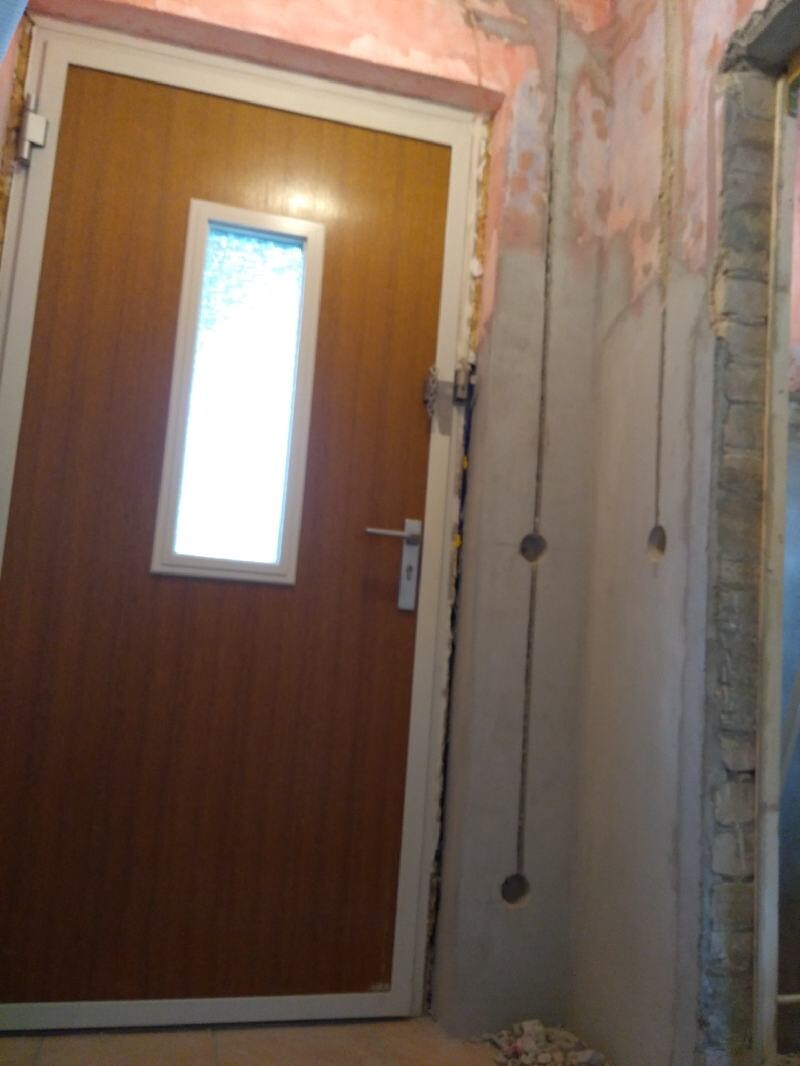 Brown wooden door with narrow window in an unfinished interior; raw walls visible.