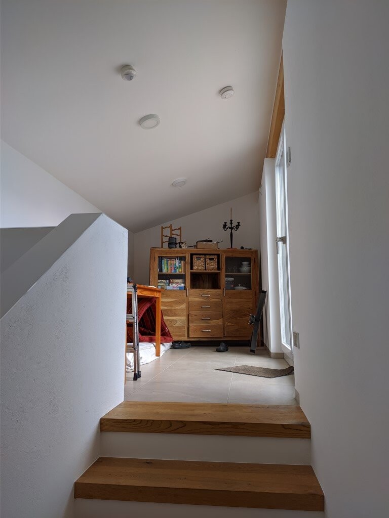 Loft room with staircase, wooden cabinet, books, window on the right; bright and tidy.