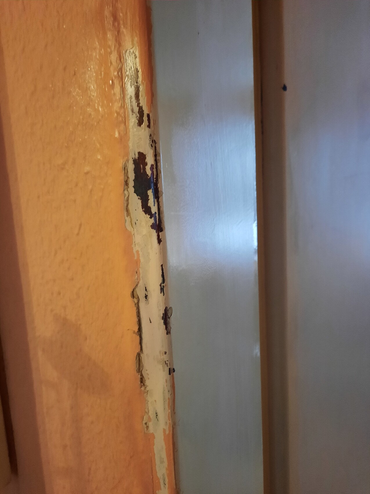Wooden door frame with chipped orange paint layer next to light metal part.