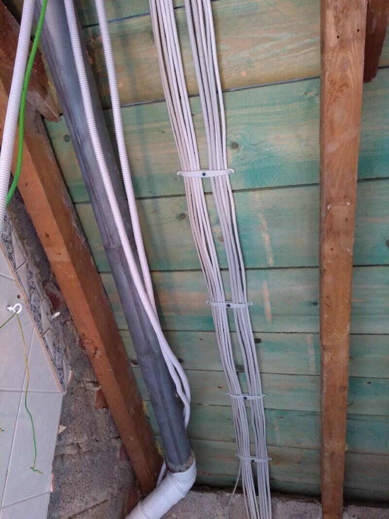 Multiple cables and pipes fixed with cable ties on a green-painted wooden wall.