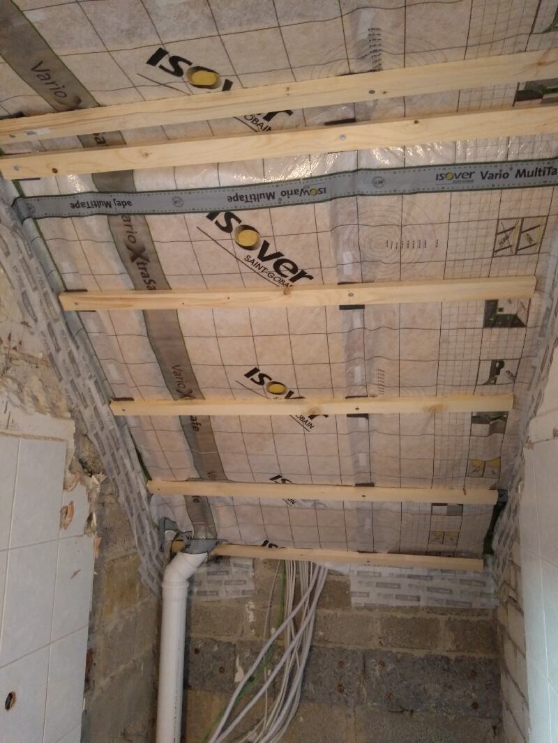 Ceiling under construction with wooden battens, Isover insulation, PVC pipe and cable bundles on the wall.