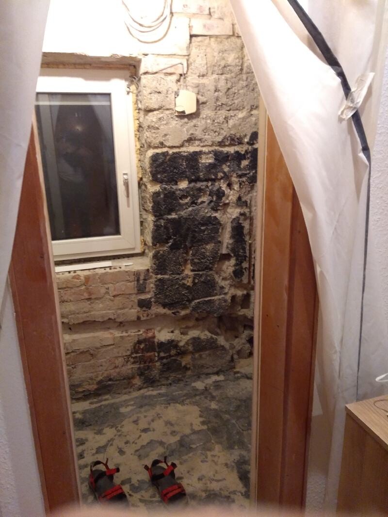 Construction area with exposed brick wall, window, construction foil and red sandals on the floor.