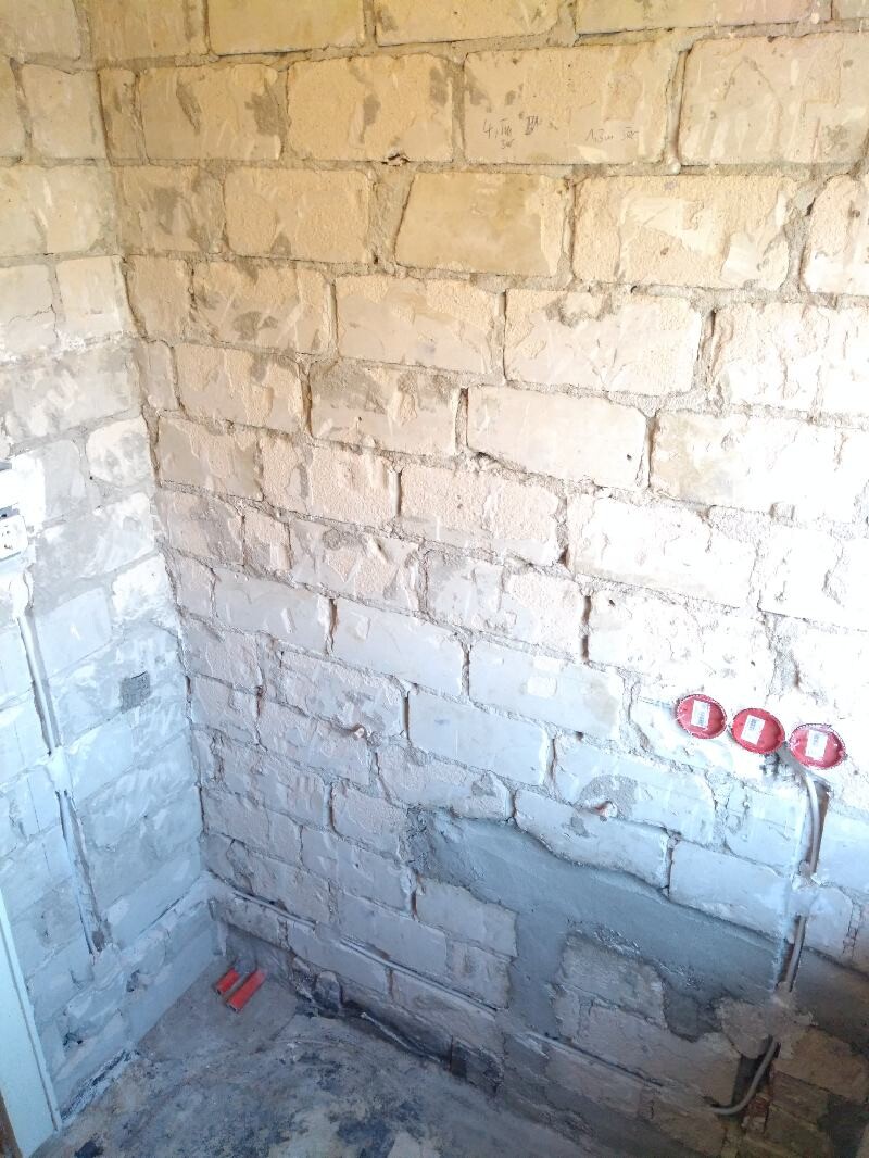 Unplastered stone wall at a construction site; three red electrical outlet covers on the wall.