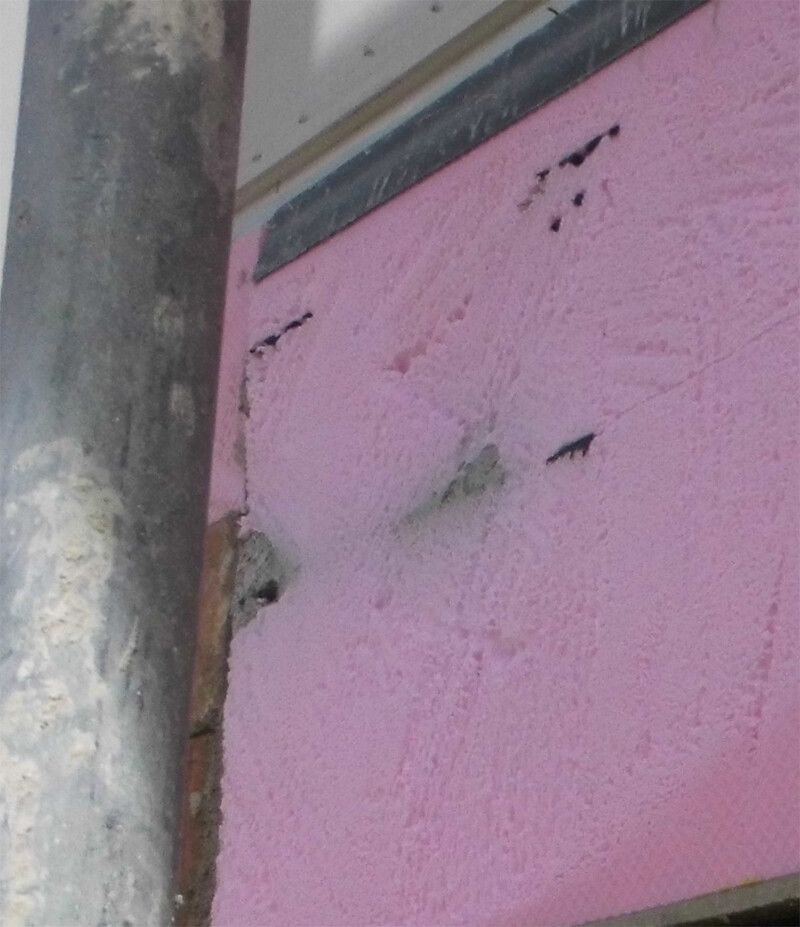 Pink insulation boards on building envelope with pipe installation at construction site