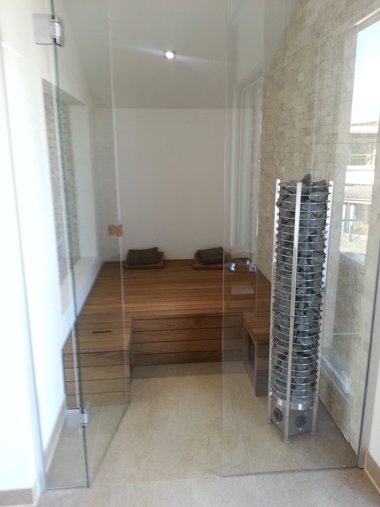 Interior of a sauna with wooden bench, glass walls, and a heater with stones.
