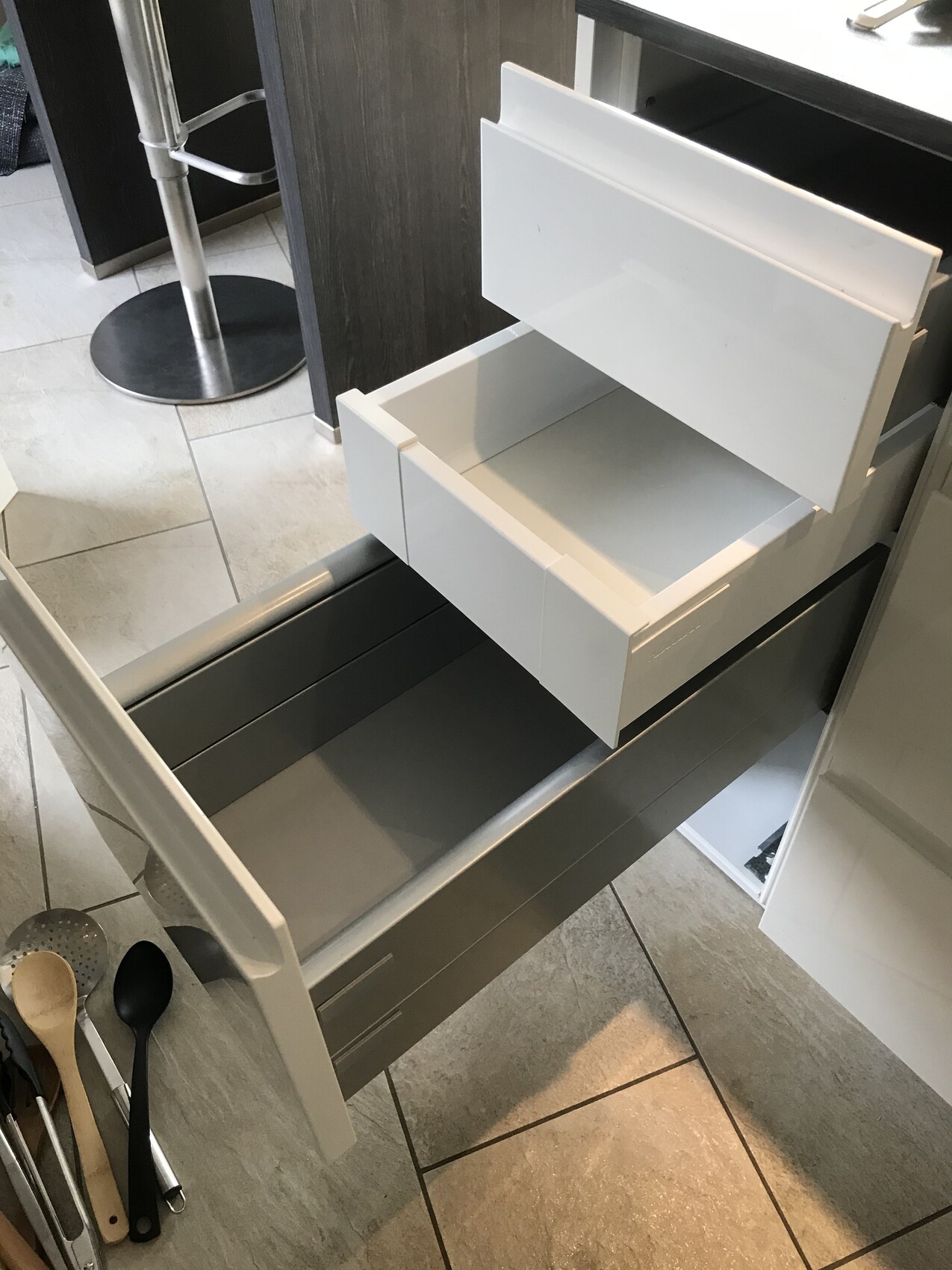 White kitchen drawers open; smaller ones on top, larger below; tools on the floor.
