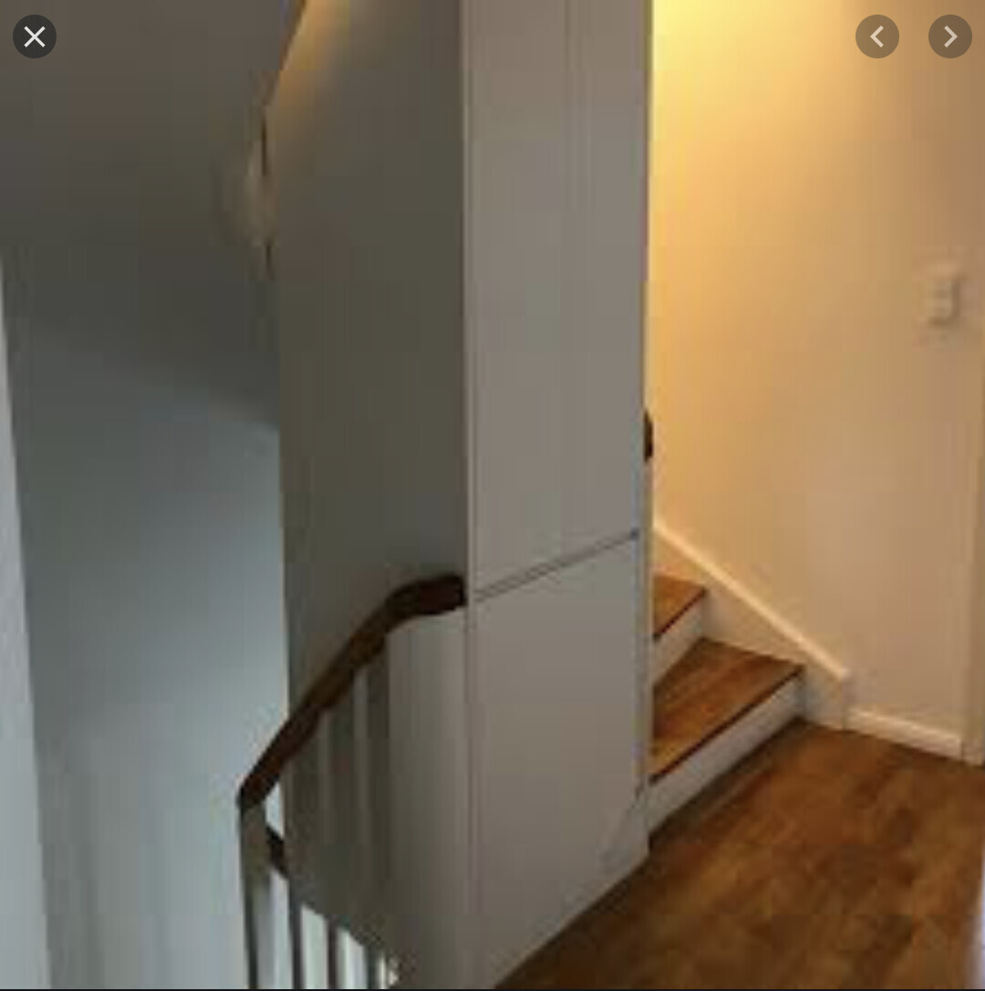 Interior view of a stairwell: wooden stairs on the right, wooden floor, white wall cabinet on the left.