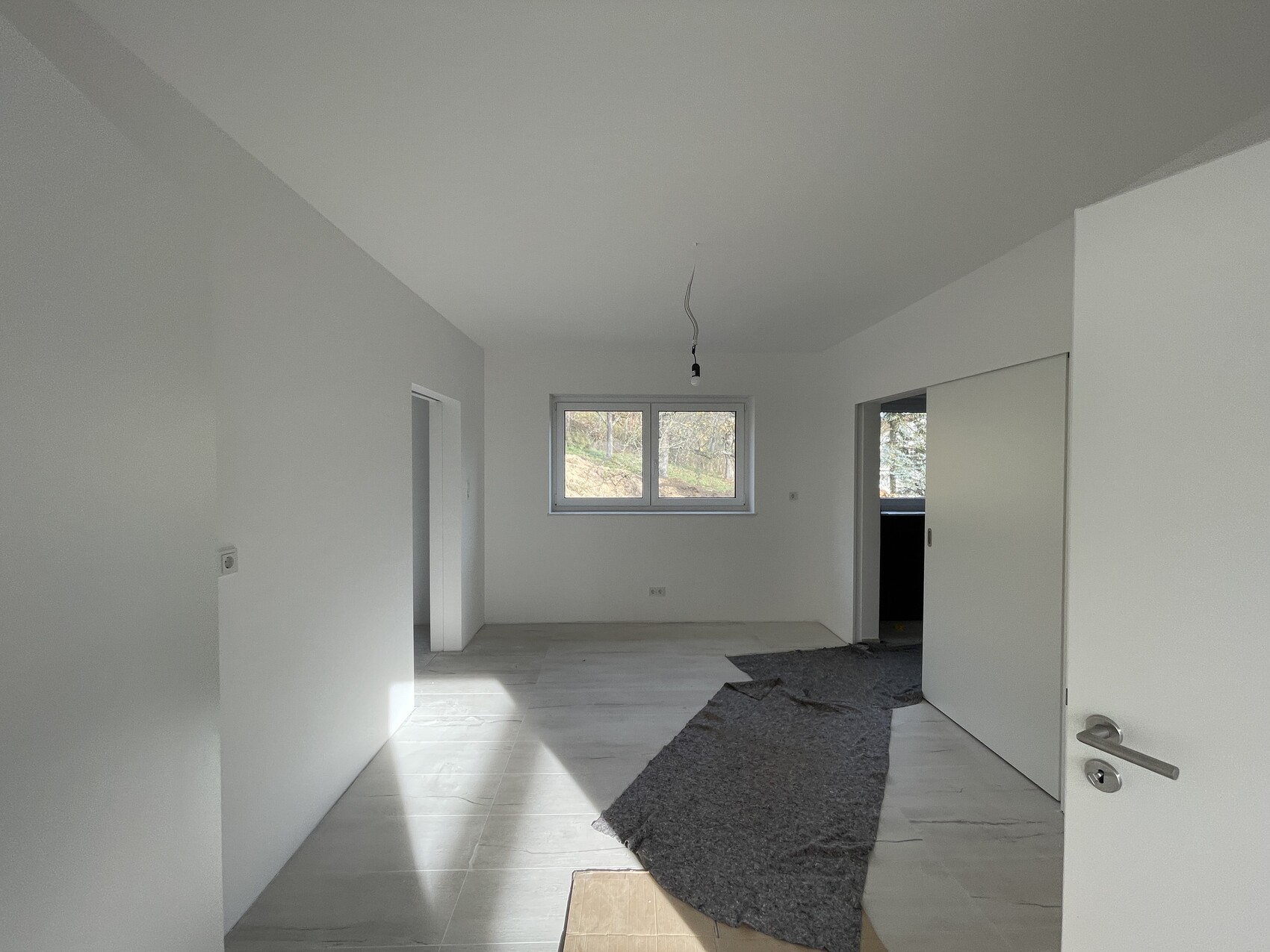 Empty new construction room with white walls, window front, open passageway, and hanging light fixture.