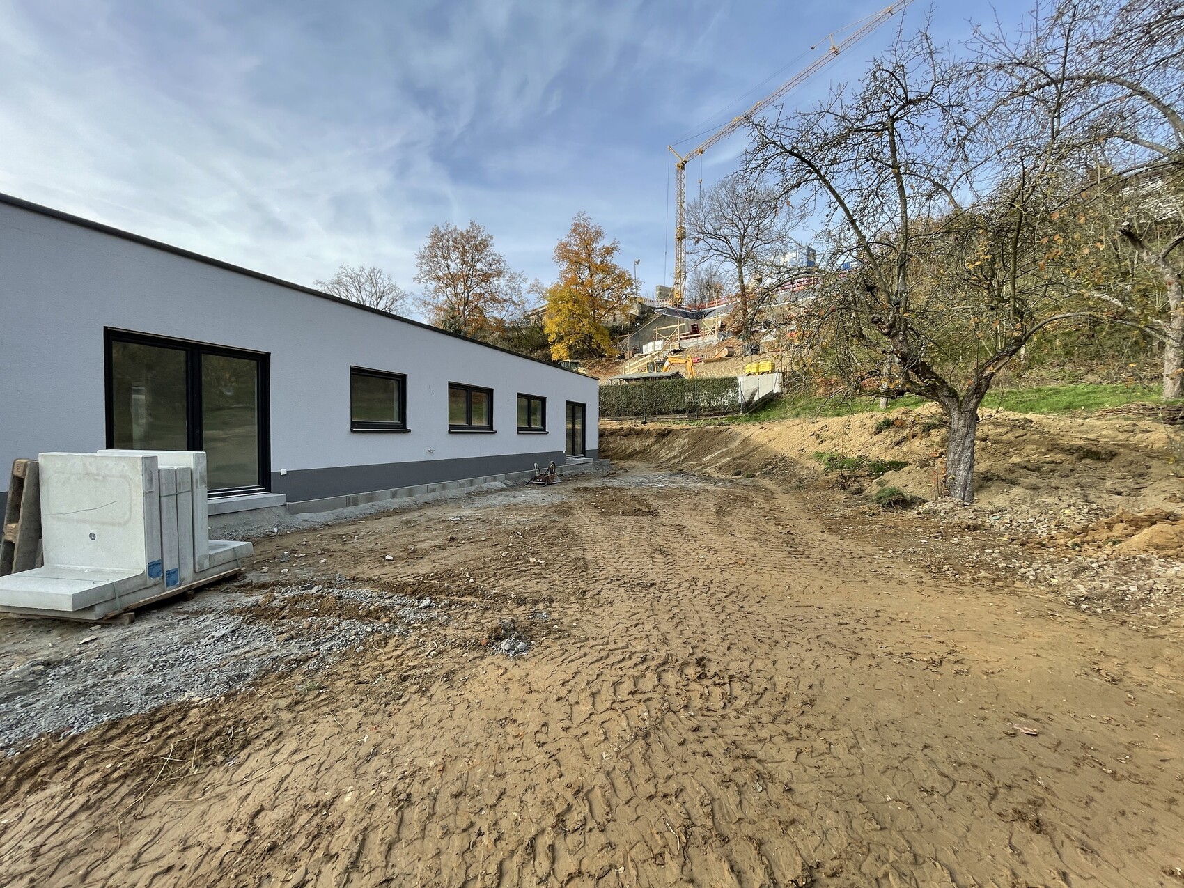 Construction site with long white building section, construction crane in the background, unpaved ground.