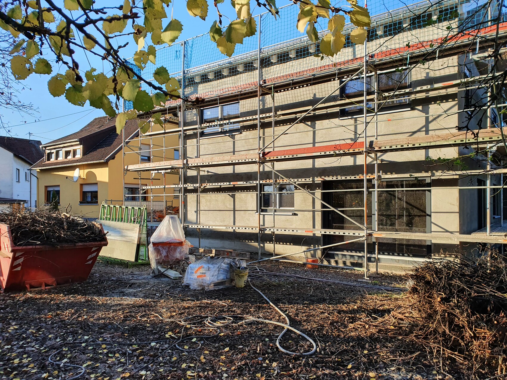 Construction site with scaffolding around a house, construction debris, bags, and autumn leaves in the yard