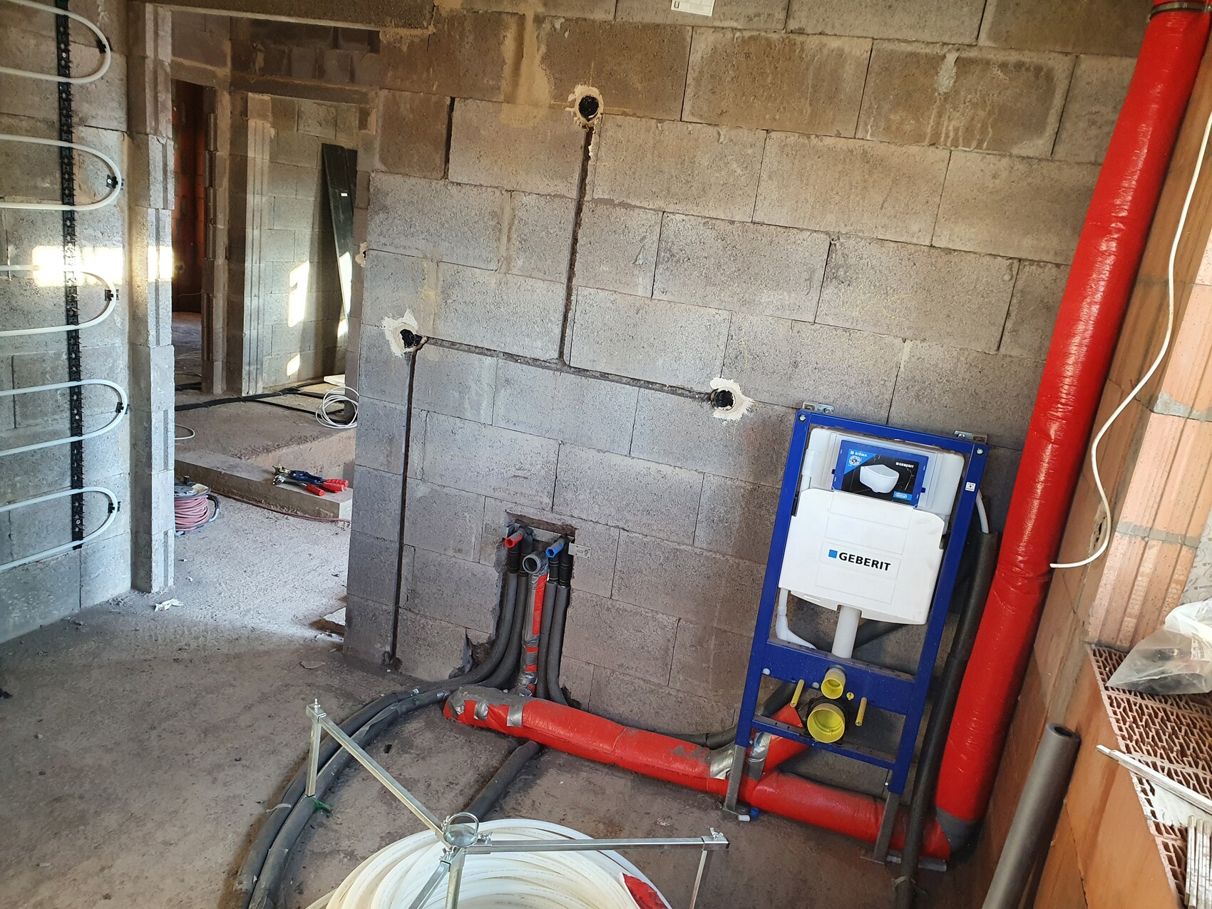 Construction site: Geberit toilet wall carrier with cistern, red pipes on concrete wall.