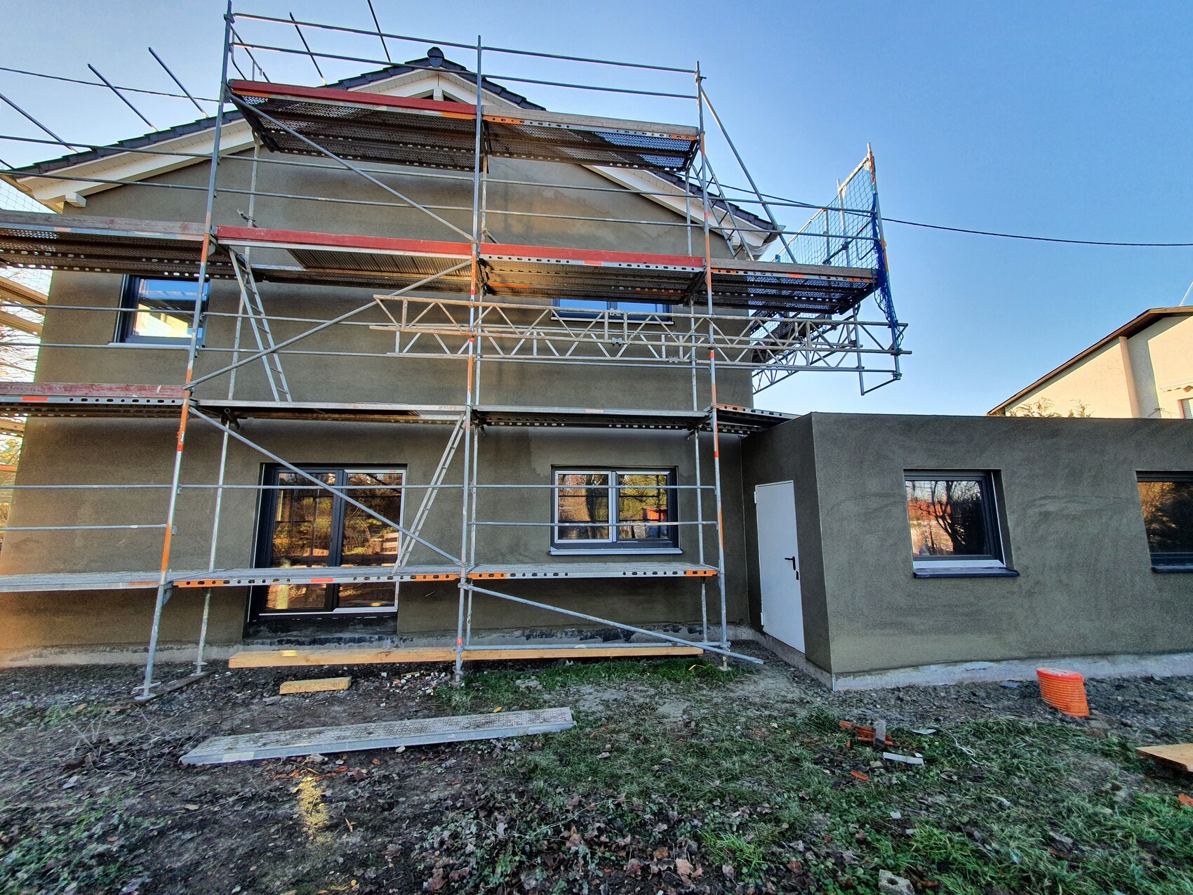 Two-story house under construction with large scaffolding, blue nets, and ongoing work.
