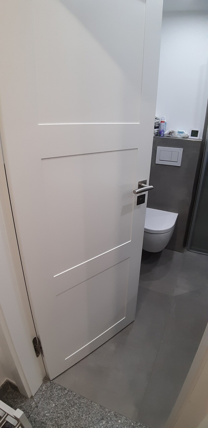 Open white door to the bathroom with toilet, cistern, and glass shower.