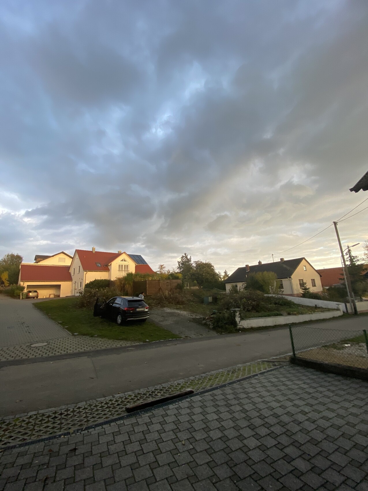 Exterior view of several houses in a suburb with street, car, and cloudy sky.