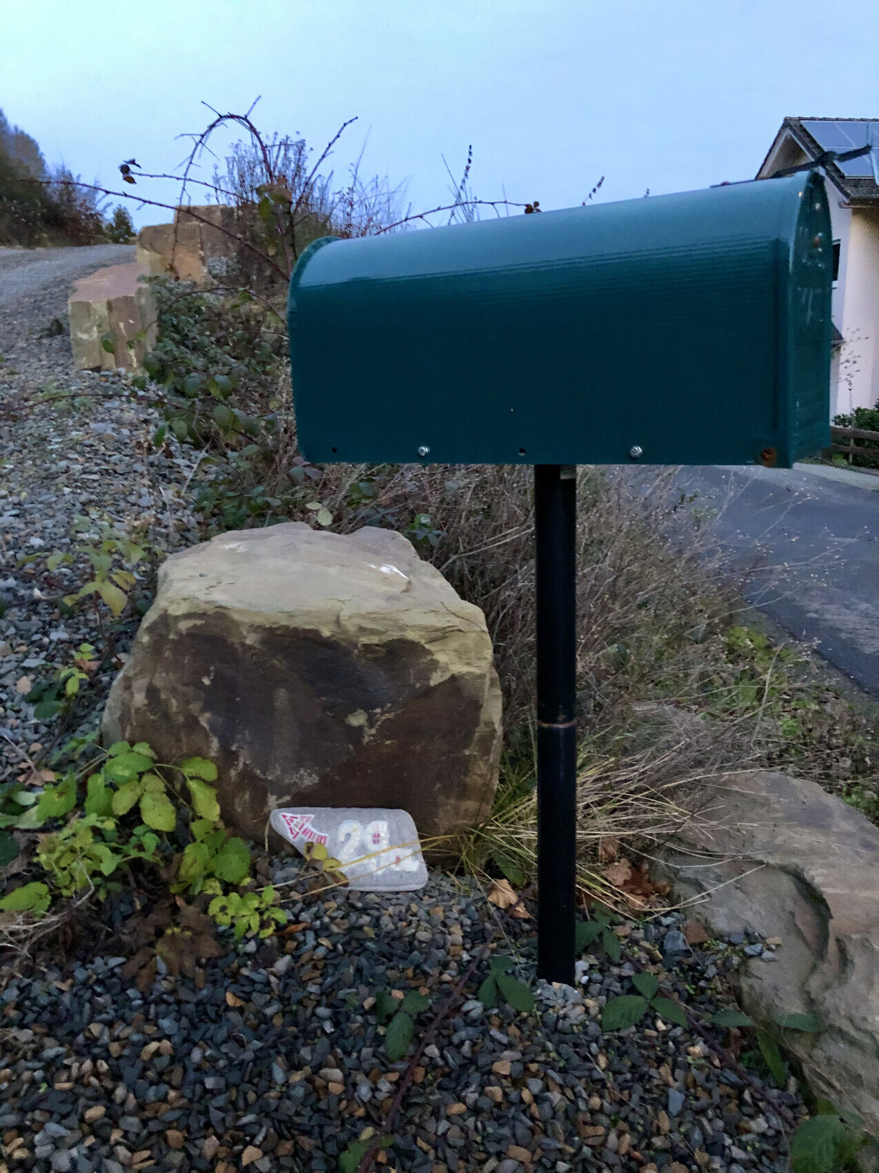 Grüner Briefkasten auf Pfosten im Vorgarten neben Kiesweg und Steinblock