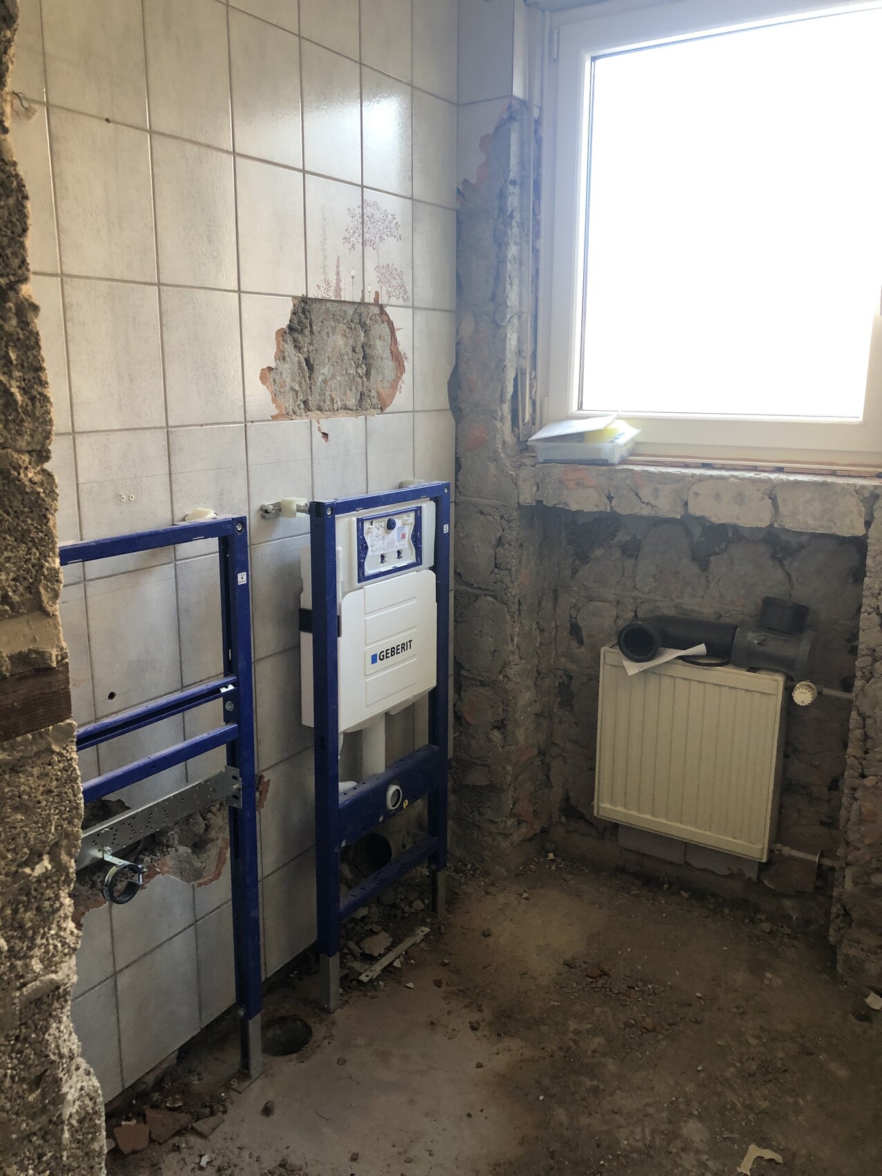 Badezimmer im Rohbau mit blauem Geberit-Wandrahmen, offener Wand und Fliesen.