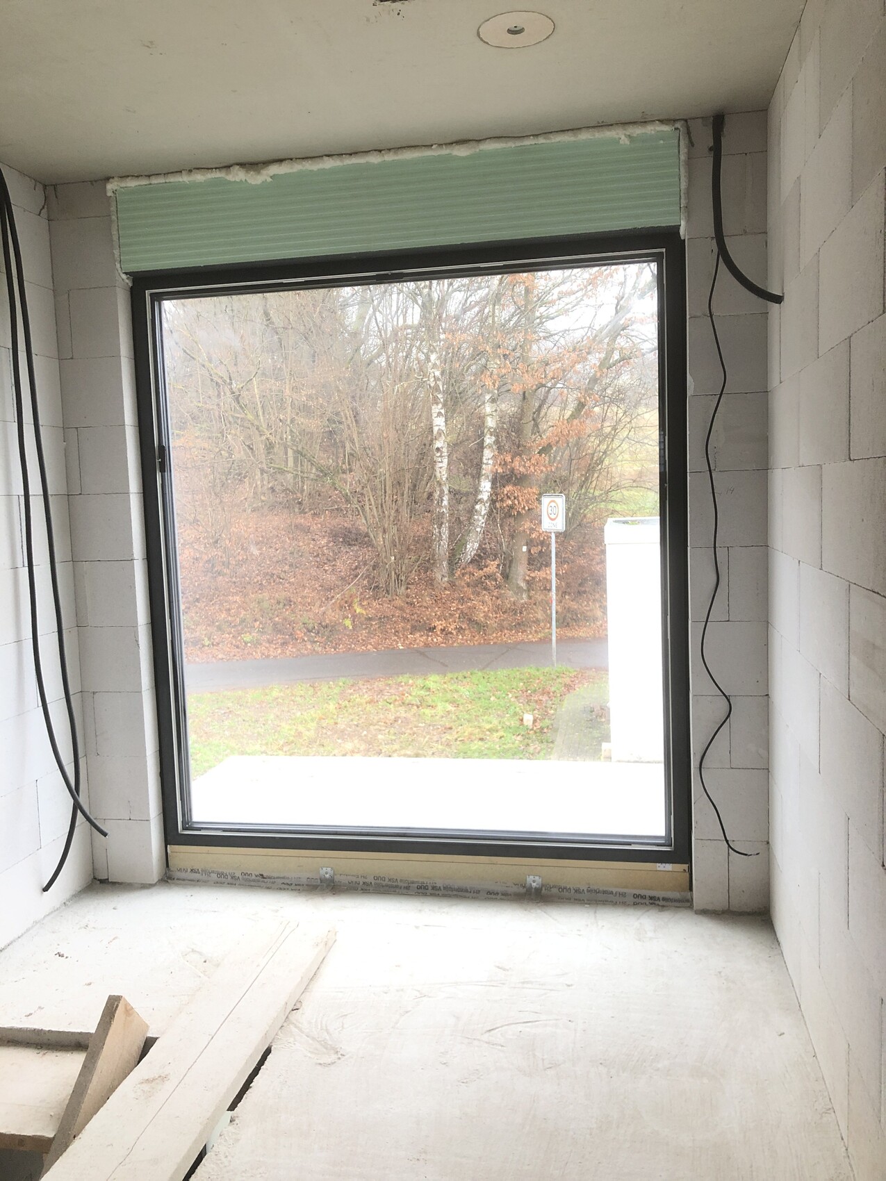 Unfinished interior with large window, view outside to trees, street, and 30 km/h (18.6 mph) sign.
