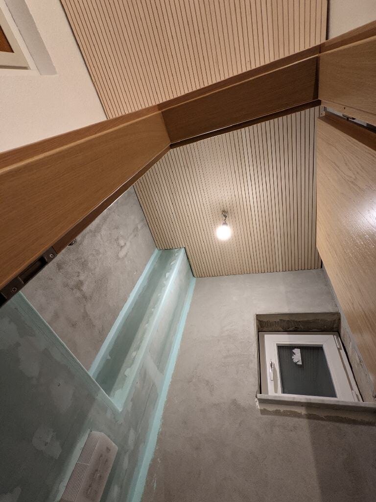 Bathroom corner with glass shower, wooden panels on ceiling and wall, window.