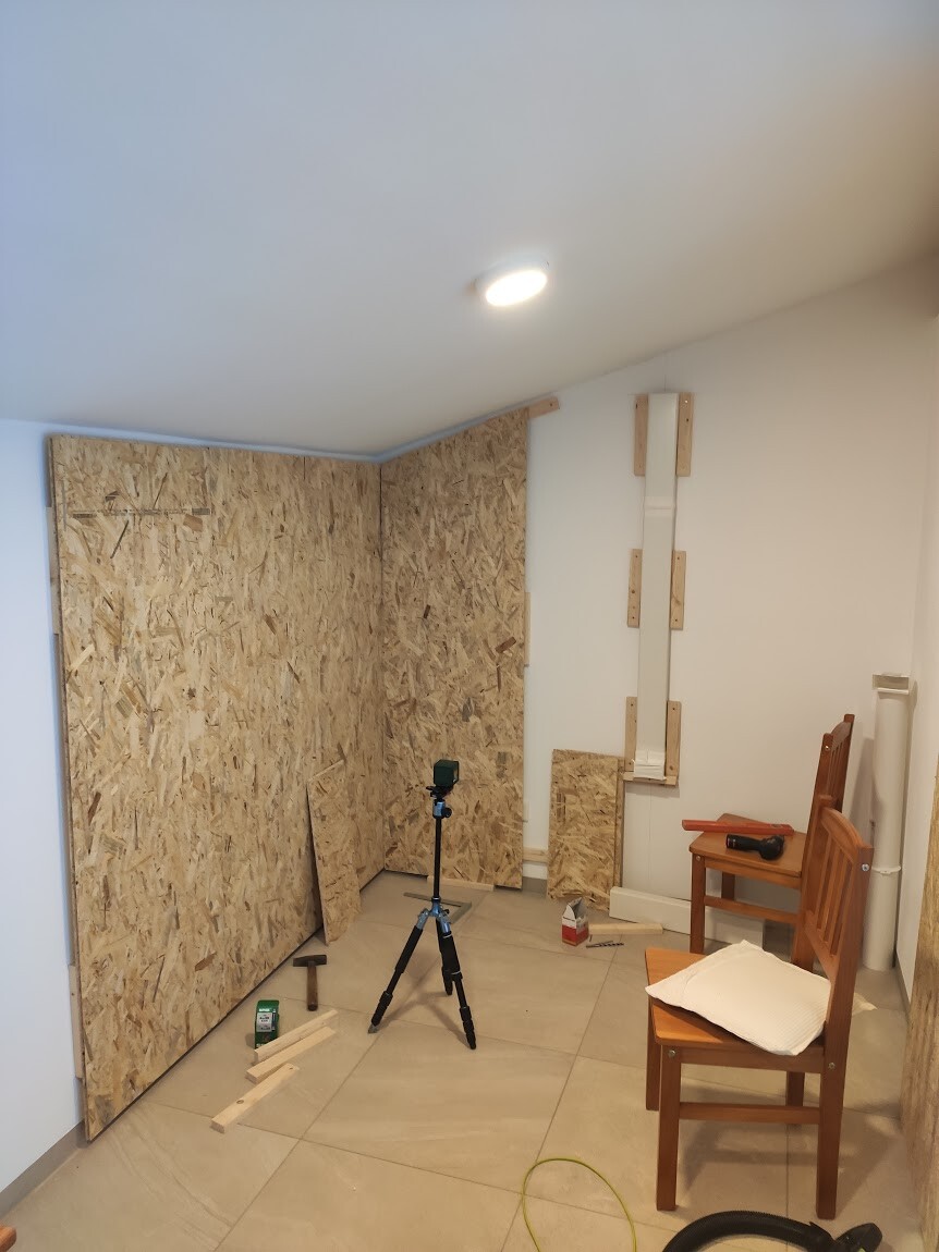 Interior workshop with OSB walls, tripod camera, wooden panels, and two chairs.