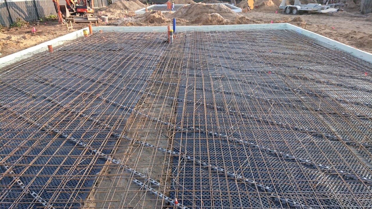 Construction site with reinforcing steel mesh for concrete floor; pipes protruding vertically.