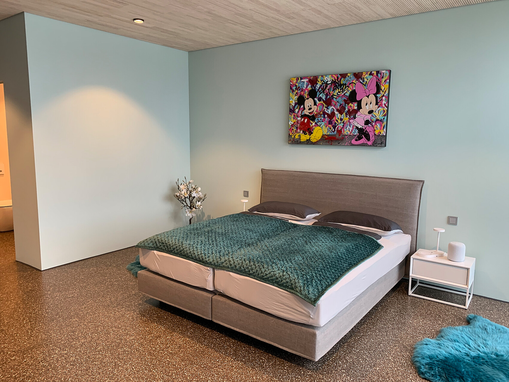 Bedroom with mint-colored walls, bed with gray headboard, Minnie/Mickey painting.